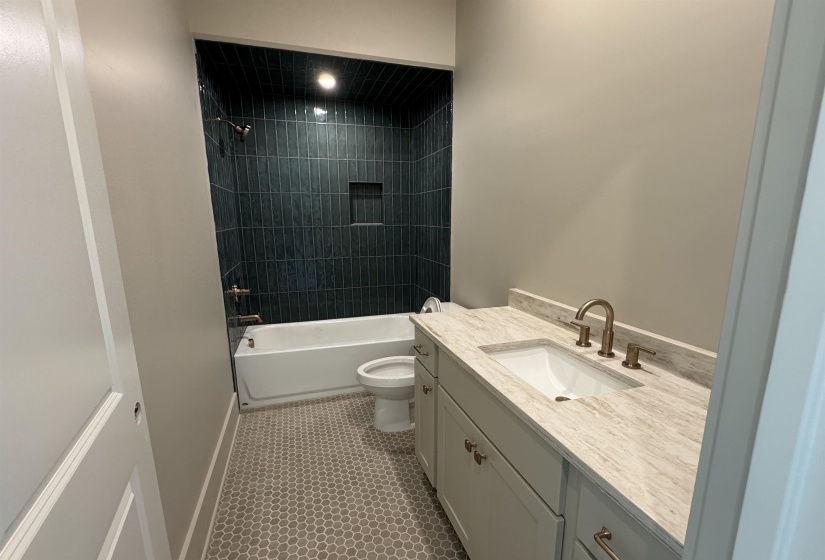 Bathroom featuring a built-in tub with a dark tile surround and recessed niche, a vanity with a light-toned countertop, an undermount sink, and a bronze-finish faucet