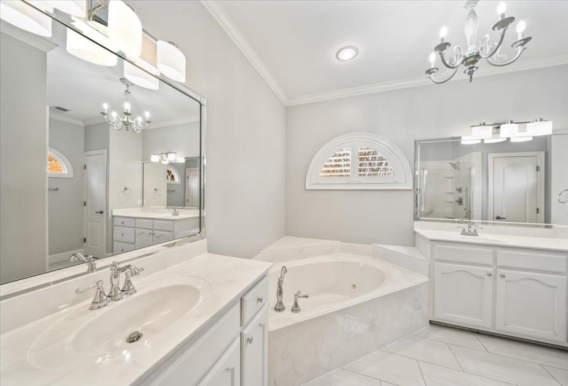 Full bathroom featuring hanging lights, ornamental molding, a shower stall, two vanities, and a garden tub