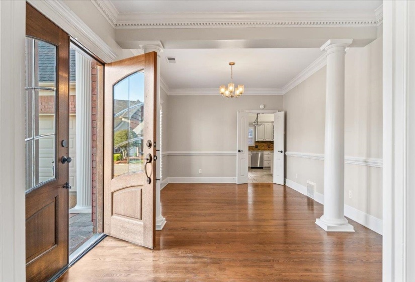 Entryway featuring crown molding, wood finished floors, suspended lighting, and ornate columns