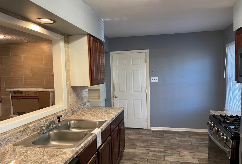Kitchen featuring stainless steel gas stove, wood finish floors, dark wood finish cabinetry, and backsplash