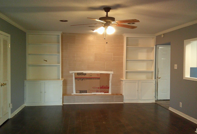 Unfurnished living room with built in shelves, crown molding, ceiling fan, and dark wood finished floors