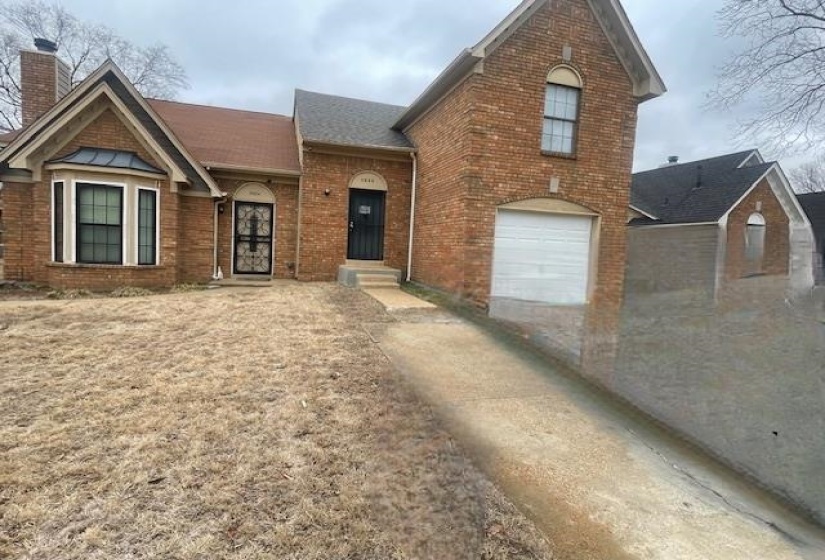 View of front of property featuring brick siding, driveway, an attached garage, and a chimney