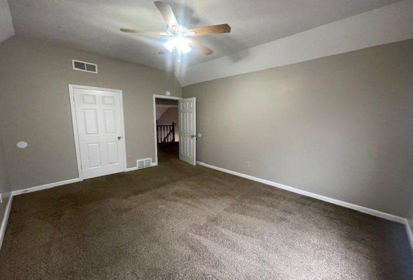 Unfurnished bedroom featuring lofted ceiling, dark carpet, and ceiling fan