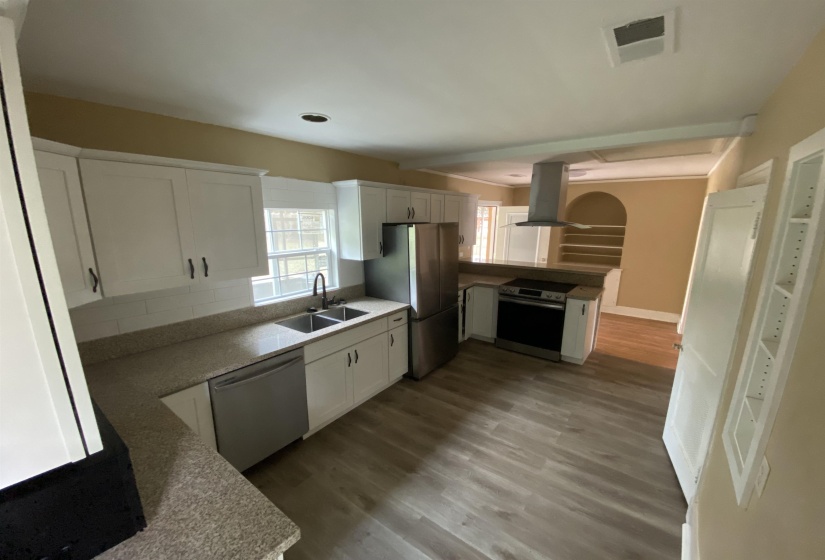 Kitchen with stainless steel appliances, white cabinets, island range hood, dark wood finished floors, and light stone countertops