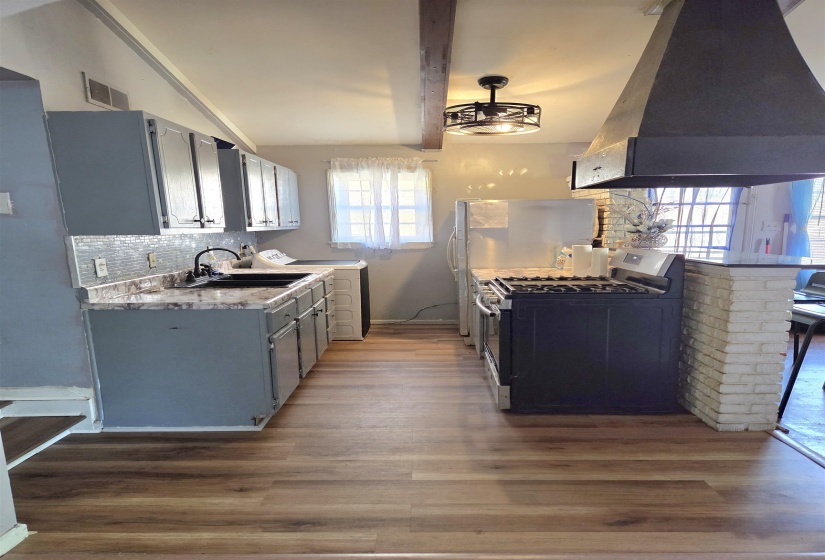 Kitchen with backsplash, light countertops, gray cabinetry, stainless steel appliances, and extractor fan