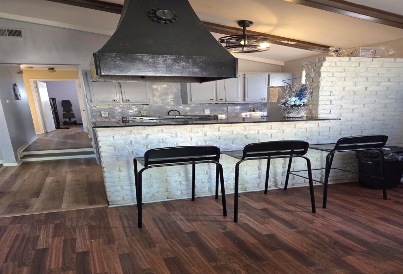 Kitchen with dark countertops, tasteful backsplash, vaulted ceiling with beams, dark wood-type flooring, and a breakfast bar area