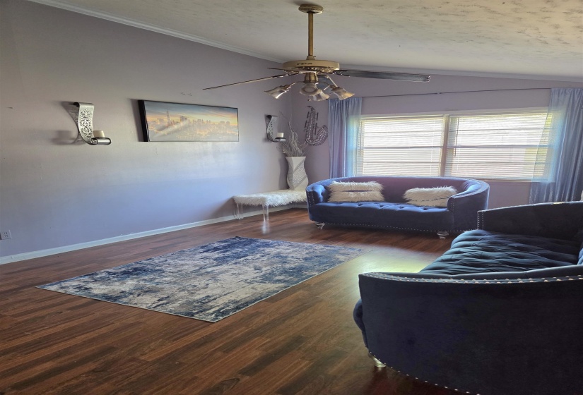 Living area featuring vaulted ceiling, ceiling fan, dark wood finished floors, and ornamental molding