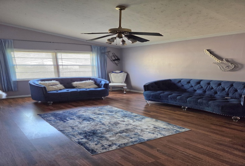 Living room with dark wood-style flooring, a ceiling fan, and ornamental molding