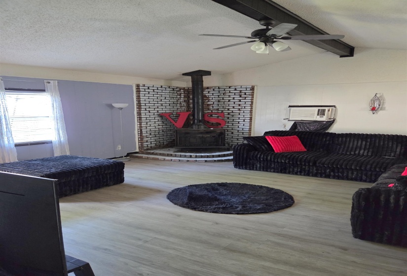 Living area with a wood stove, ceiling fan, beam ceiling, a textured ceiling, and wood finished floors