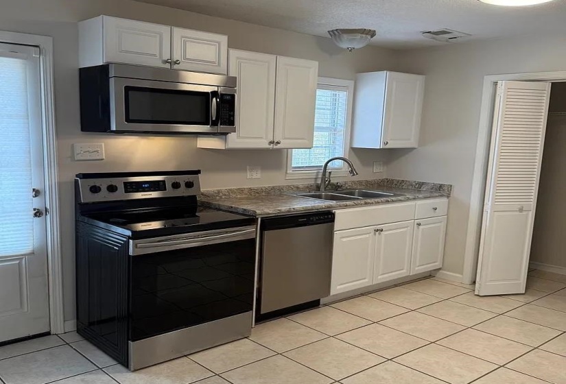 Kitchen with stainless steel appliances, white cabinets, dark countertops, and light tile patterned floors