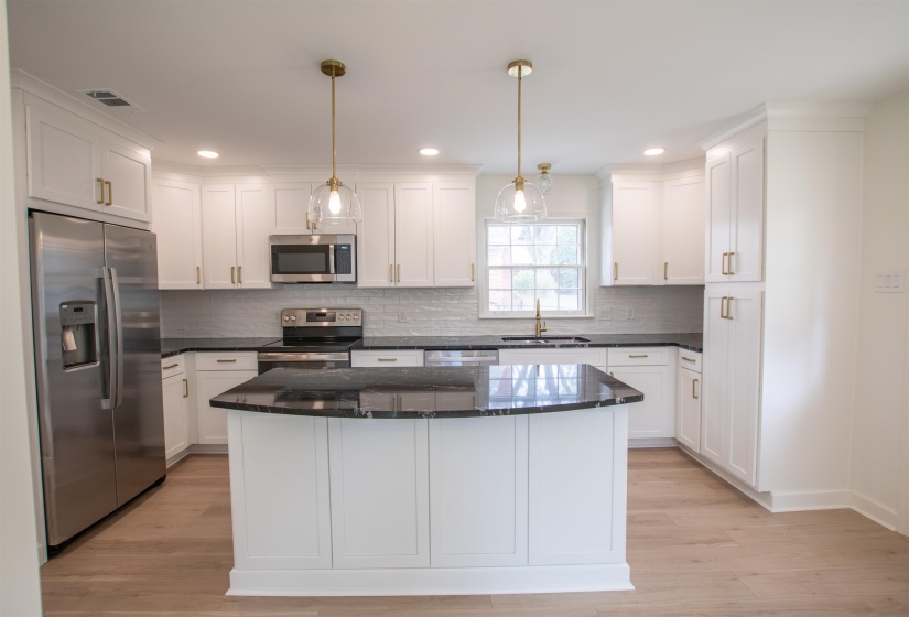 Kitchen with light wood-style flooring, stainless steel appliances, large island with overhang and granite countertops