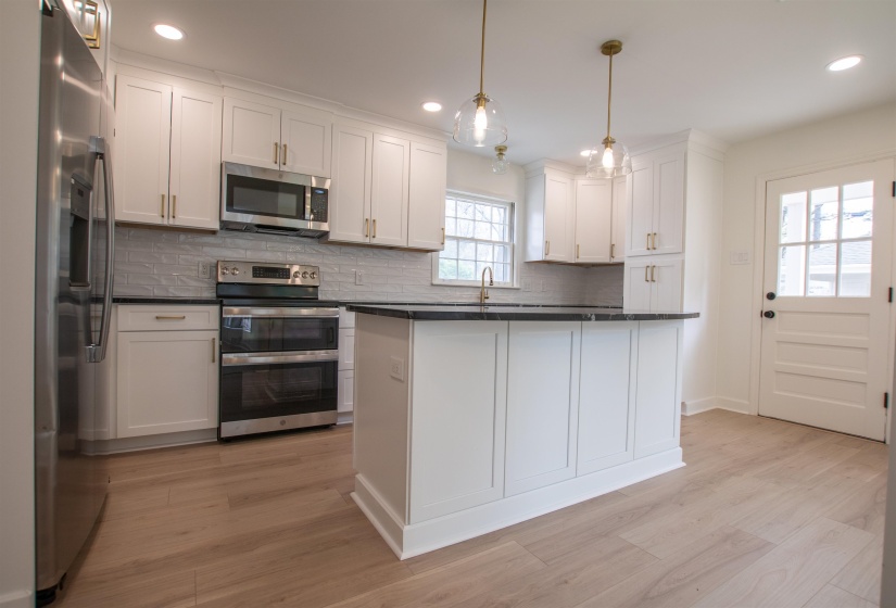 Kitchen with a sink, granite countertops, appliances with stainless steel finishes, white cabinetry, and backsplash