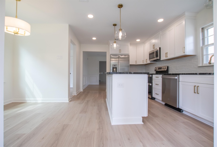 Kitchen with light wood-style floors, white cabinets, a center island, appliances with stainless steel finishes, and granite countertops