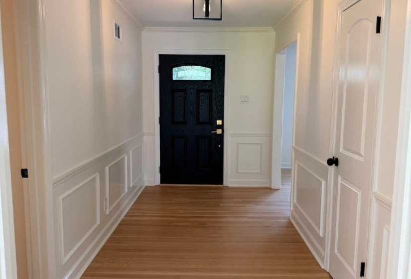 Entryway featuring wood-finish flooring, wainscoting, crown molding, a dark wood-finish front door with an arched glass inset, and a contemporary ceiling light fixture