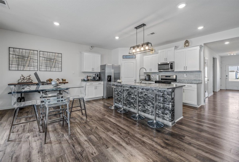 Kitchen featuring white cabinets, a center island with sink, a breakfast bar, stainless steel appliances, and light stone countertops
