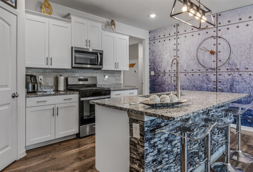 Kitchen with stainless steel appliances, dark wood-style floors, light stone countertops, and white cabinets