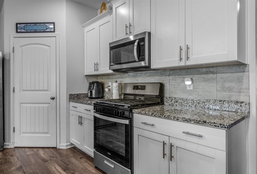 Kitchen with stainless steel appliances, dark stone counters, white cabinetry, dark wood-style floors, and tasteful backsplash
