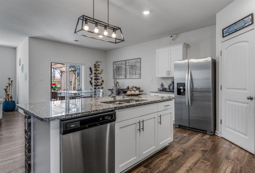 Kitchen with stainless steel appliances, dark wood finished floors, a kitchen island with sink, dark stone counters, and white cabinets