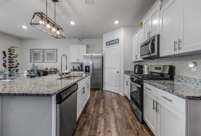Kitchen featuring stainless steel appliances, light stone countertops, a kitchen island with sink, dark wood-type flooring, and white cabinets