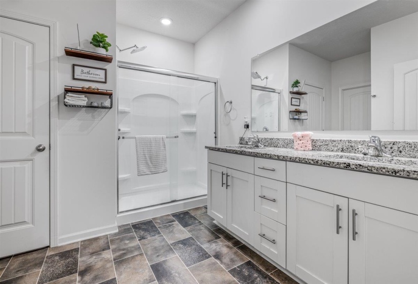 Bathroom with double vanity, a stall shower, and stone finish floors