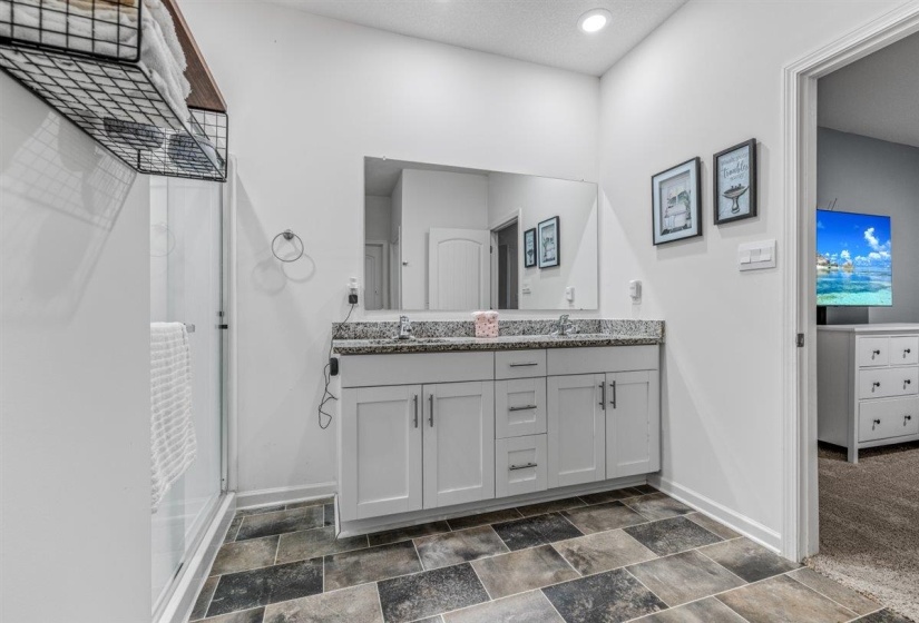Full bath featuring double vanity, a stall shower, stone finish floors, and recessed lighting