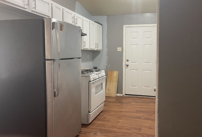 Kitchen with freestanding refrigerator, white gas range, dark wood-style floors, white cabinetry, and a textured ceiling