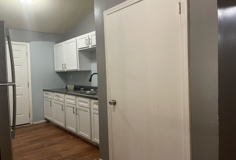 Kitchen with dark countertops, dark wood-type flooring, freestanding refrigerator, and white cabinetry