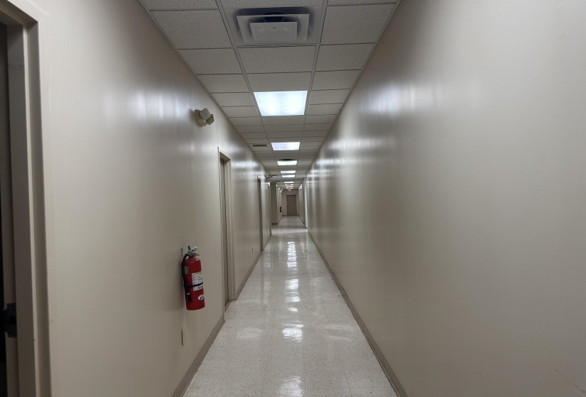 Corridor with light floors, a drop ceiling, visible vents, and baseboards