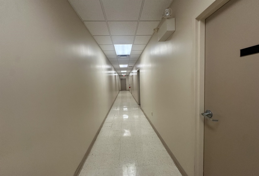 Corridor with a paneled ceiling, light floors, and baseboards