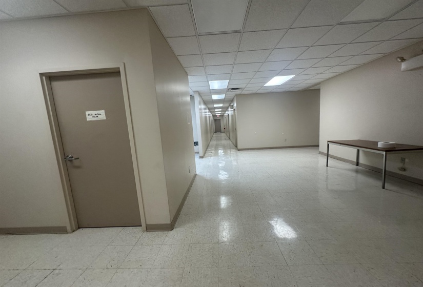 Corridor with light floors, a drop ceiling, and baseboards