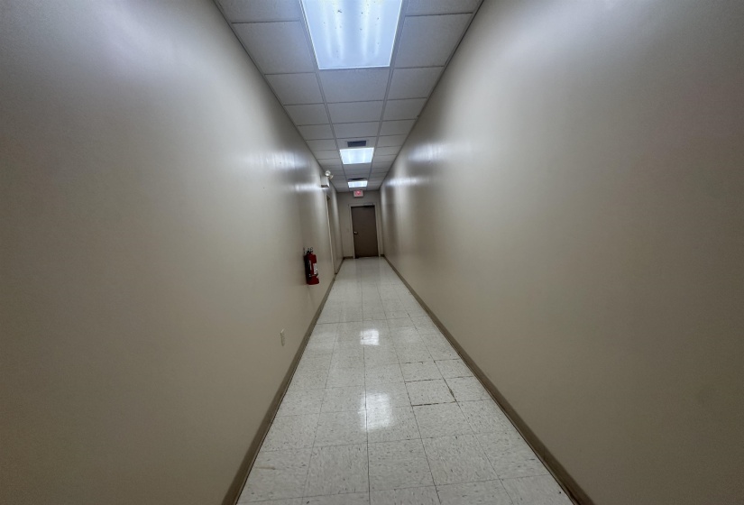 Hallway featuring light floors, a drop ceiling, and baseboards