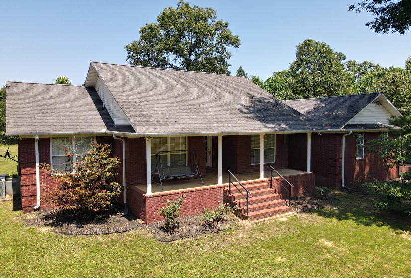 Brick exterior featuring a covered front porch with white columns and a gray asphalt shingle roof