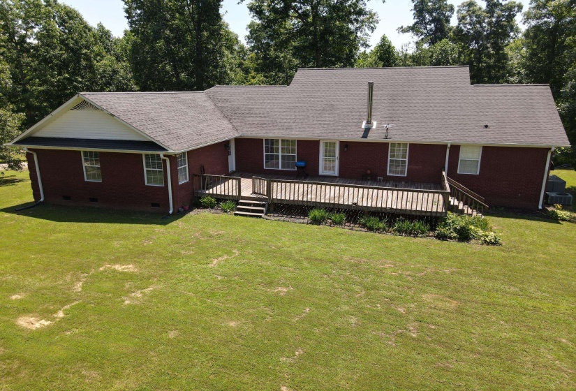 Rear exterior featuring an expansive wood deck with railing and stairs to the lawn
