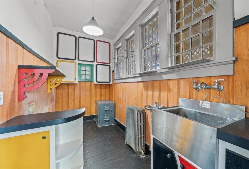 Bar with dark countertops, wood walls, radiator, glass insert cabinets, and hanging light fixtures