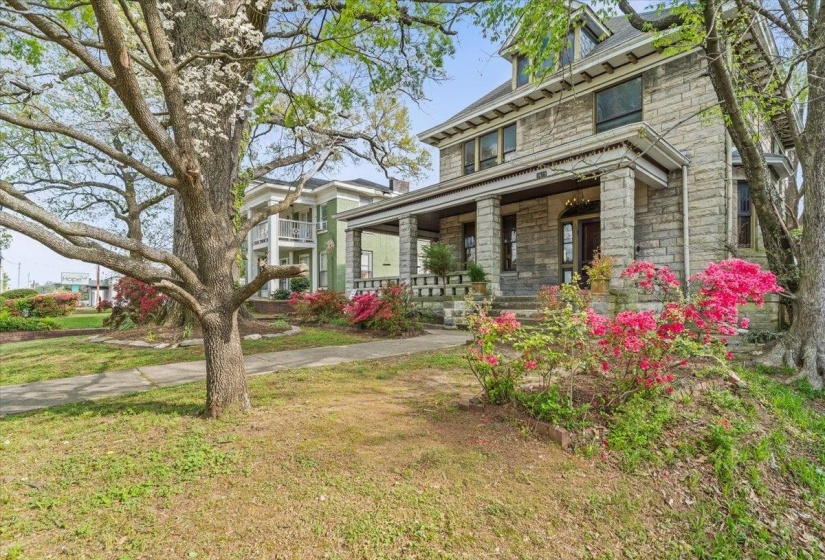 American foursquare style home featuring a porch, stone siding, and a front lawn