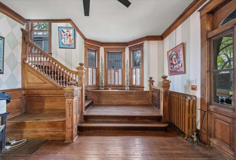 Stairs with ornamental molding, a wainscoted wall, hardwood / wood-style flooring, ceiling fan, and wood walls