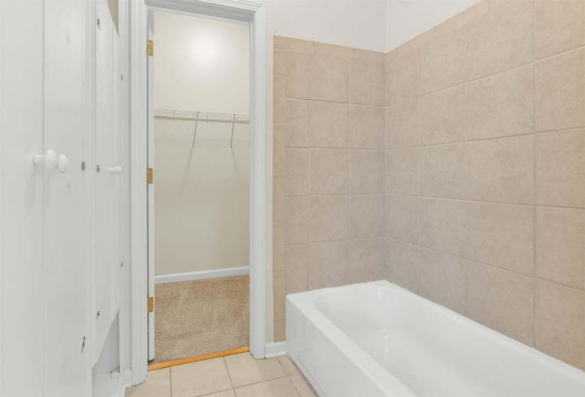 Bathroom with a spacious closet, a bath, and light tile patterned floors