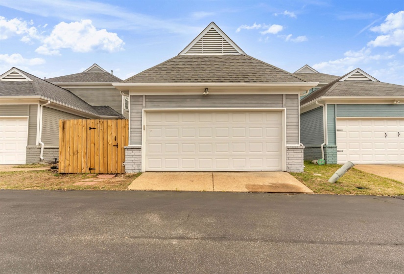 View of front of home with a garage, brick siding, roof with shingles, and a gate