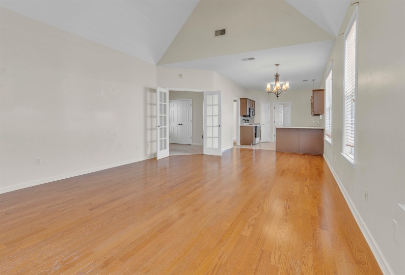 Unfurnished living room with suspended lighting, light wood-style floors, vaulted ceiling, and french doors