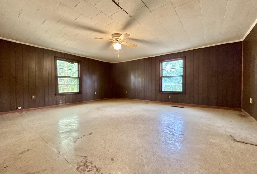 Unfurnished room with healthy amount of natural light, concrete flooring, ceiling fan, wood walls, and ornamental molding