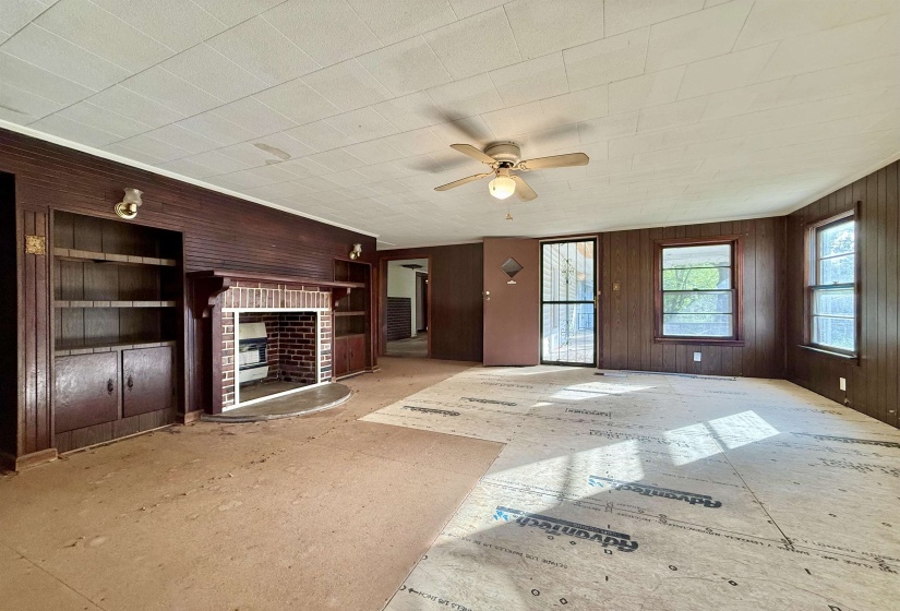 Unfurnished living room featuring wooden walls, a ceiling fan, and a brick fireplace