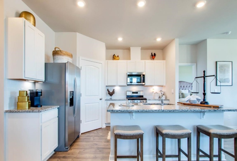 Kitchen with white cabinetry, a kitchen breakfast bar, light stone countertops, backsplash, and stainless steel appliances
