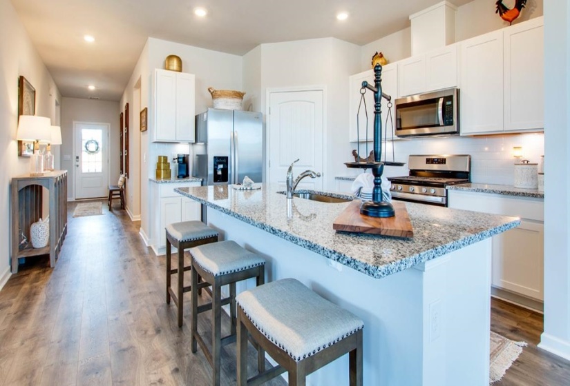 Kitchen featuring a kitchen island with sink, stainless steel appliances, light stone counters, dark wood finished floors, and a kitchen breakfast bar