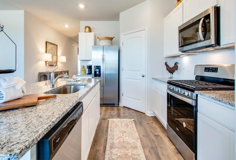Kitchen featuring stainless steel appliances, white cabinetry, light wood finished floors, light stone countertops, and backsplash