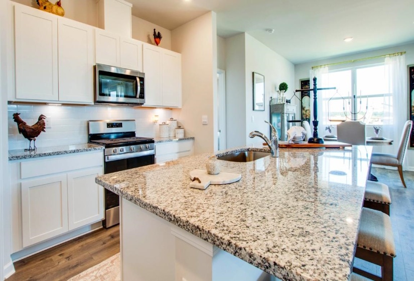 Kitchen featuring stainless steel appliances, a kitchen bar, light wood-type flooring, white cabinets, and light stone countertops