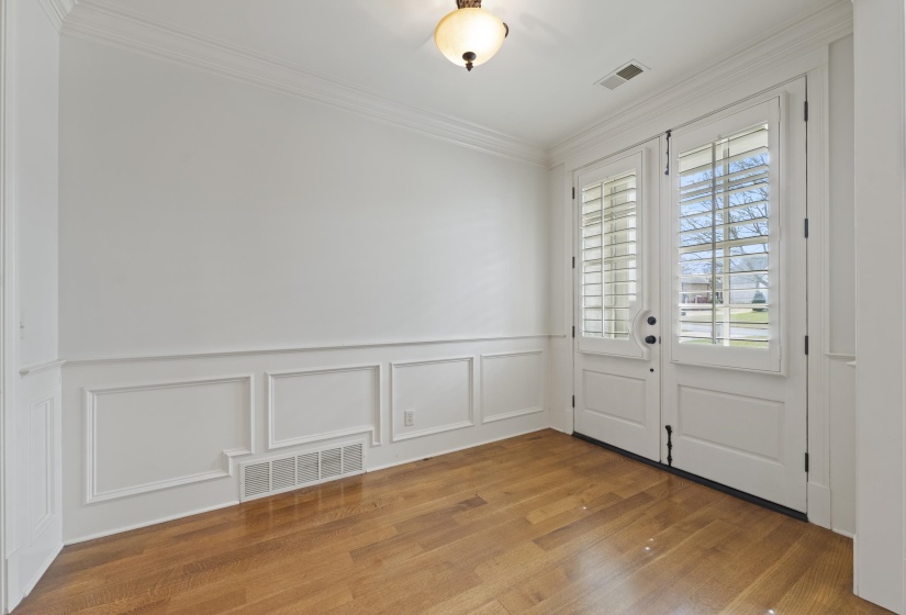 Foyer with wood finished floors, ornamental molding, wainscoting, and a decorative wall