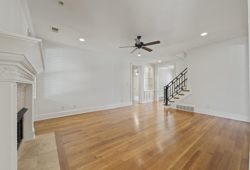 Unfurnished living room with built in shelves, a fireplace, light wood-style floors, ceiling fan, and crown molding