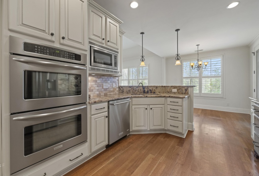 Kitchen with stainless steel appliances, light stone counters, hanging lights, dark wood-style floors, and a peninsula