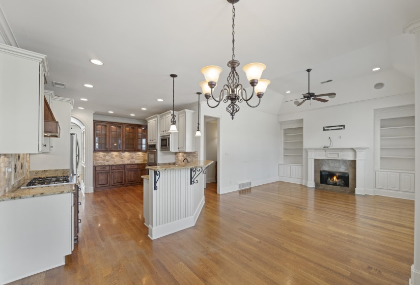 Two tone kitchen featuring light stone countertops, built in features, hanging lights, a kitchen breakfast bar, and glass insert cabinets