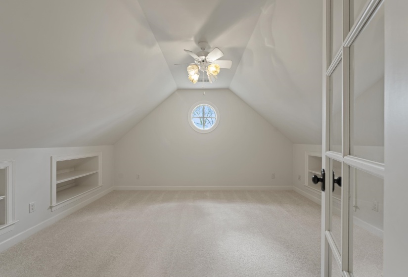 Bonus room featuring built in shelves, light carpet, and ceiling fan
